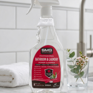 SMG Professional Series Bathroom and Laundry Power Cleaner 500ml spray bottle on a wooden bathroom countertop next to a gold tap and grey towel.